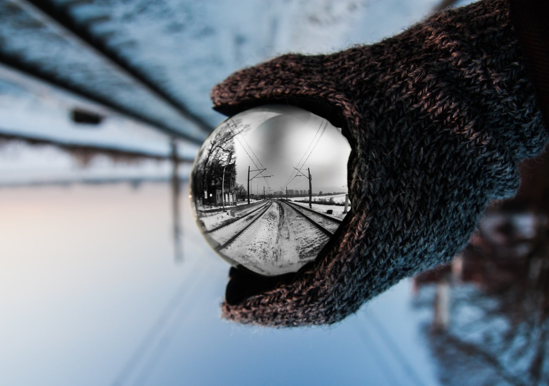 Gloved hand holding a mirrored ball in the snow between two train tracks