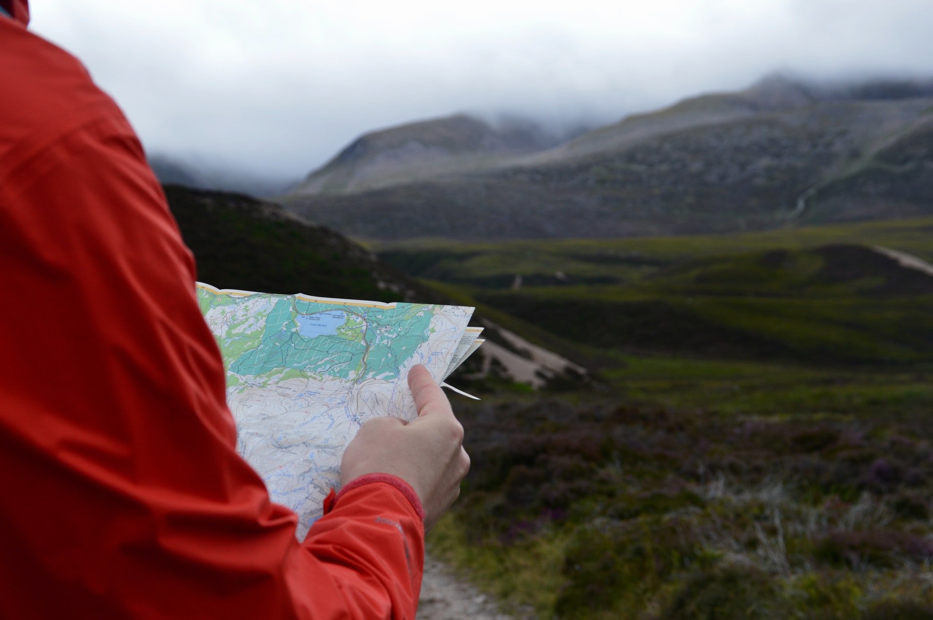 Person in red jacket holding map in front of foggy mountains